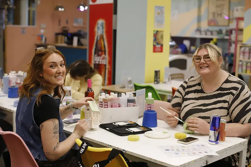 Two women smiling as they paint pottery at a table in the studio