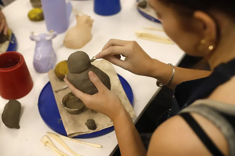 Hands shaping a small clay sculpture with a modelling tool