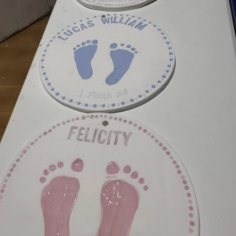 Two glazed keepsake plates with pink baby footprints and names