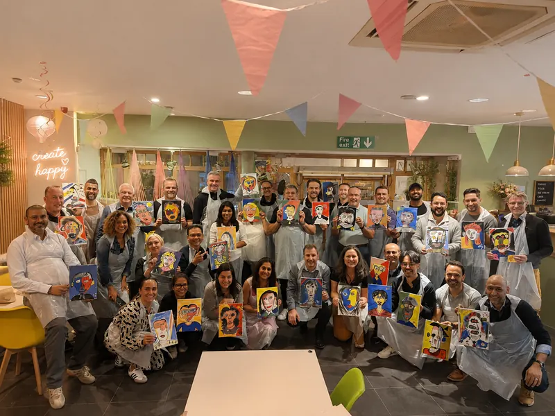 A large group of adults holding up their finished canvas paintings in the studio