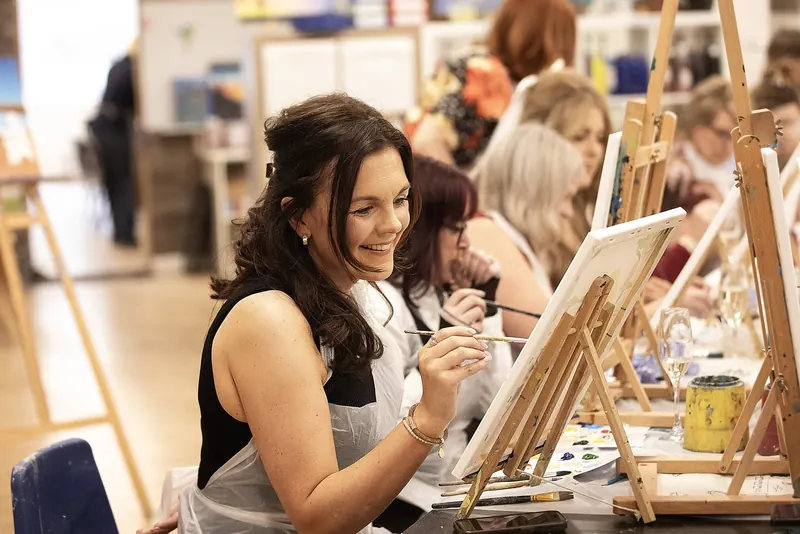 Adults painting canvases on easels at an evening painting party